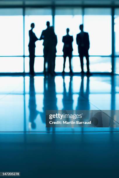 silhouette of business people standing at lobby window - business people in silhouette stock pictures, royalty-free photos & images