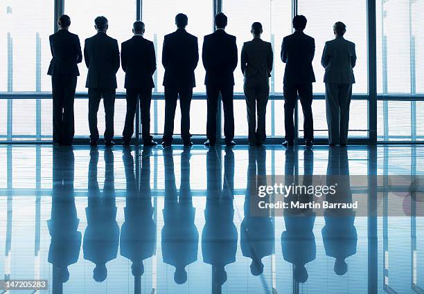 silhouette of business people in a row looking out lobby window - zakenman stockfoto's en -beelden