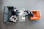 Businessmen shaking hands across coffee table in office lobby