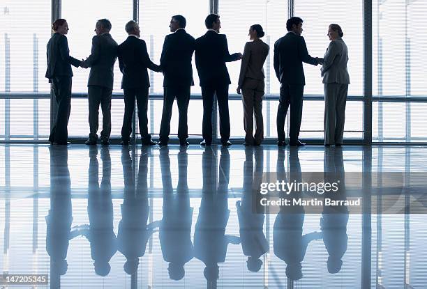 business people shaking hands in a row at lobby window - handshake silhouette stock pictures, royalty-free photos & images