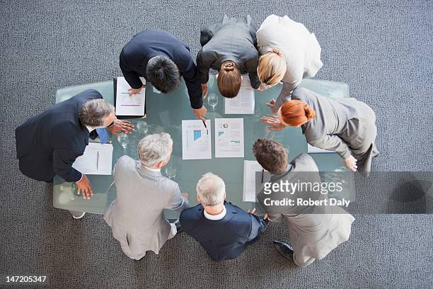 business people huddled around paperwork on table - business strategy stock pictures, royalty-free photos & images