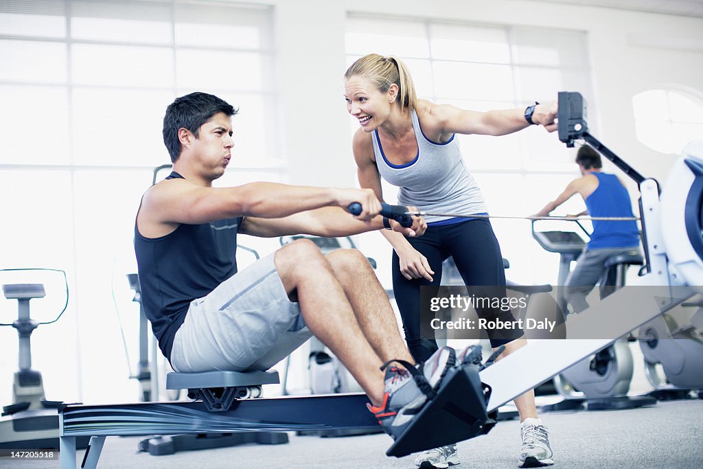 Personal trainer with man on rowing machine in gymnasium