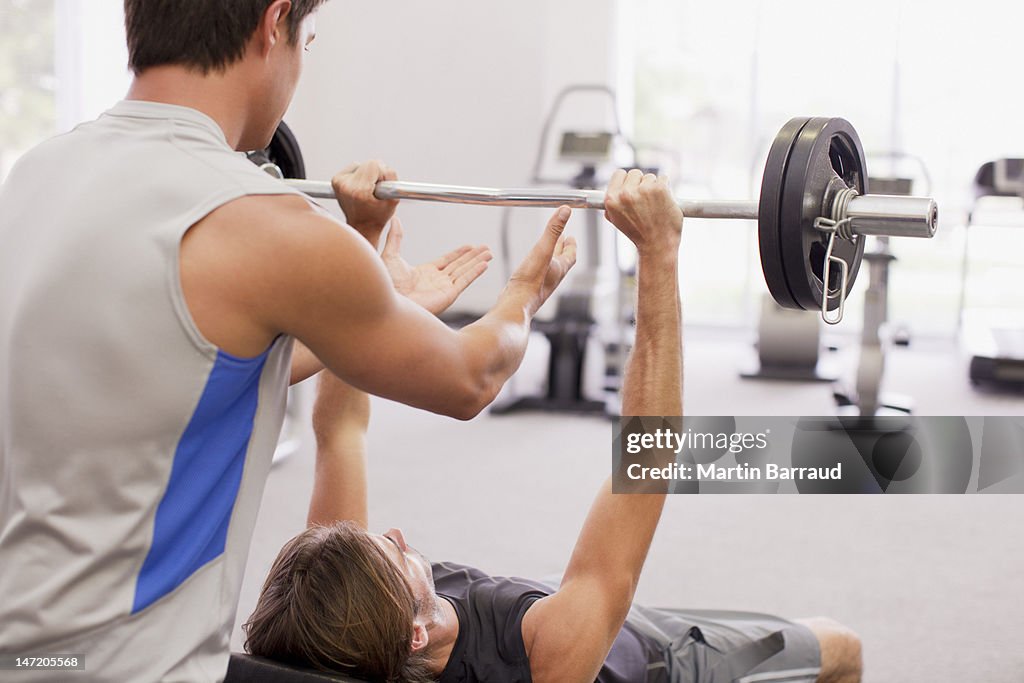 Man spotting friend lifting barbell in gymnasium