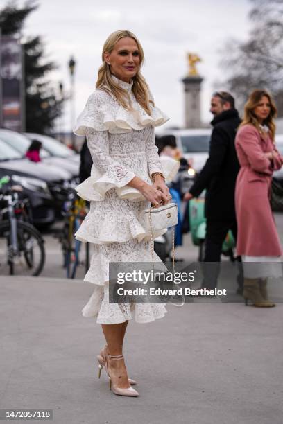Guest wears diamond earrings, a white lace cut-out print pattern high neck / long sleeves / ruffled midi dress, gold bracelets, a white shiny leather...