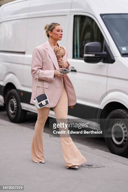 Guest wears a beige embroidered large ruffled flower high neck top, matching beige flared pants, a pale pink oversized blazer jacket, a black and...