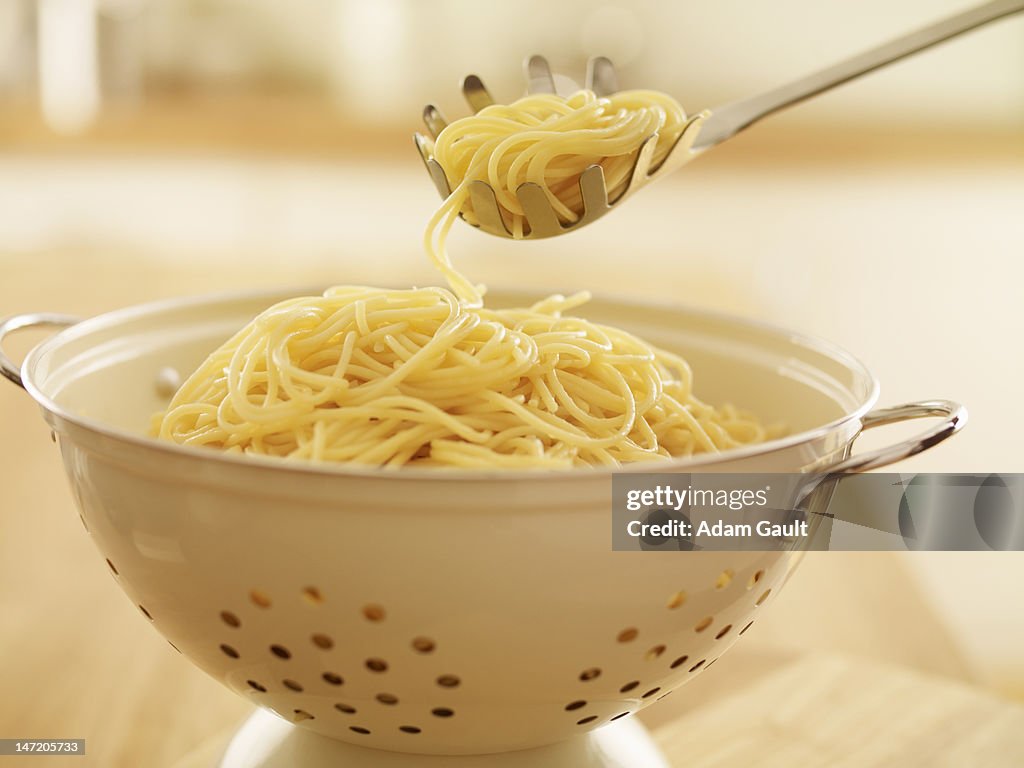 Close up of spoon scooping spaghetti in colander