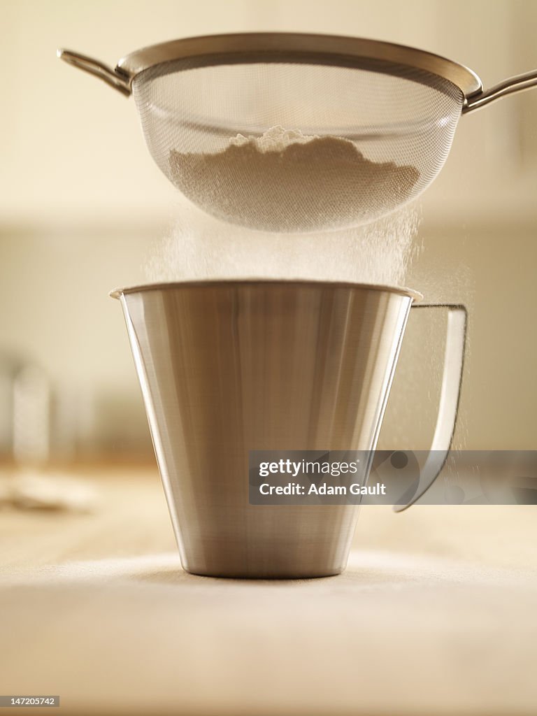 Flour being sifted into measuring cup
