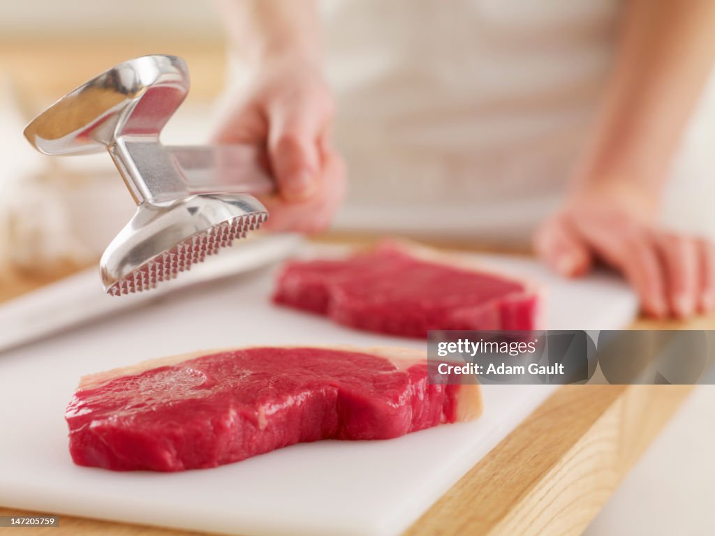 Woman holding tenderizer over raw steaks