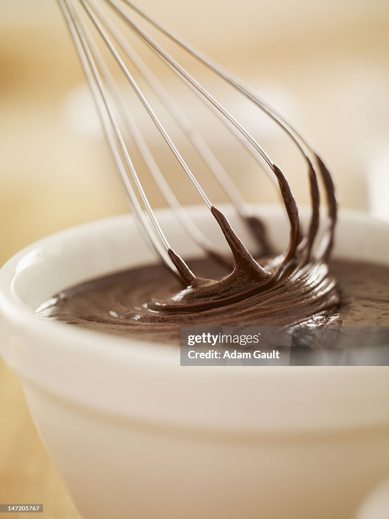 Close up of wire whisk dipping in bowl of melted chocolate