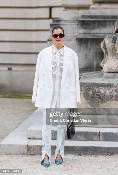 Darja Barannik wears white blazer, white blouse, blue embroidered pants with slits, pointed heels, sunglasses outside Zimmermann during Paris Fashion...