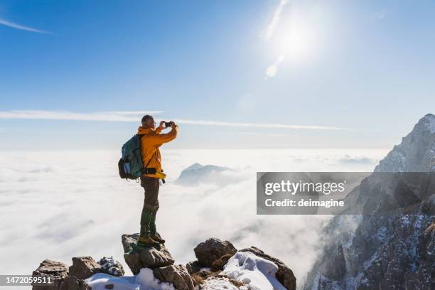 hiker with yellow rain jacket taking a pic with  smartphone in the mountains - italy argentina stock pictures, royalty-free photos & images