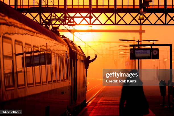 train driver waving as train departs from the hague hollands spoor station at sunset - train driver stock pictures, royalty-free photos & images