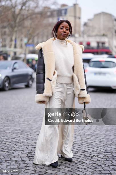 Guest wears gold earrings, a white latte wool pullover, a black matte leather with beige sheep interior and borders oversized coat, white embossed...