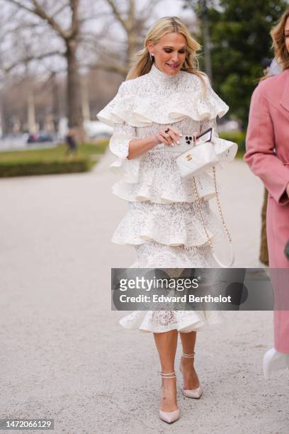 Guest wears diamond earrings, a white lace cut-out print pattern high neck / long sleeves / ruffled midi dress, gold bracelets, a white shiny leather...
