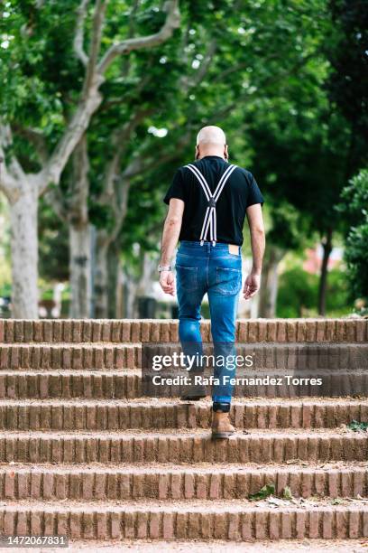 rear image of hipster man climbing stairs in a public park. - bald man stock pictures, royalty-free photos & images