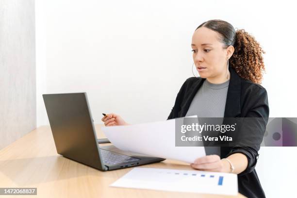 young mixed race african woman online working with laptop and paperwork at office - eingabevorrichtung stock-fotos und bilder