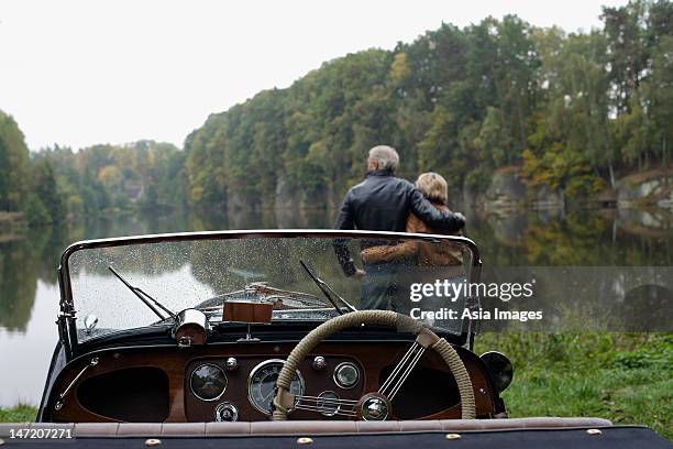 senior couple looking at lake, in front of antique car - old car stock-fotos und bilder