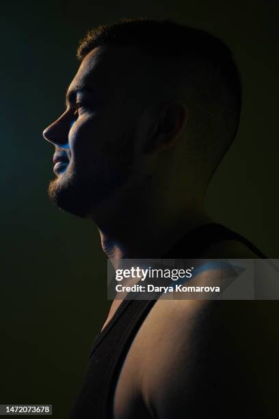 close-up portrait in profile of handsome bearded man on the black background. the sports man in undershirt with blue shadow with copy space. - smiling controluce foto e immagini stock