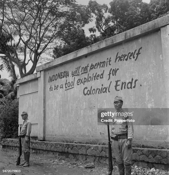 Two Imperial Japanese Army soldiers, armed with rifles, stand guard outside a walled residence on a city street in Jakarta on the island of Java,...