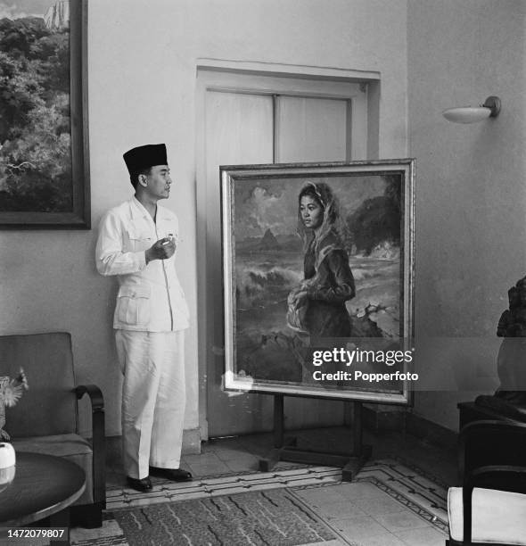 Indonesian statesman Sukarno , recently appointed President of Indonesia, stands beside a portrait painting of his wife Fatmawati at his residence,...