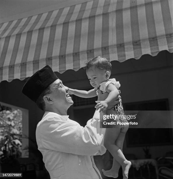 Indonesian statesman Sukarno , recently appointed President of Indonesia, holds his ten and a half month old son in the grounds of his residence,...