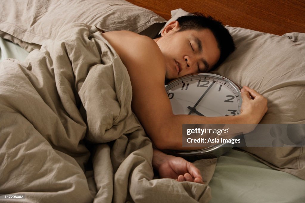 Man holding large clock in bed.