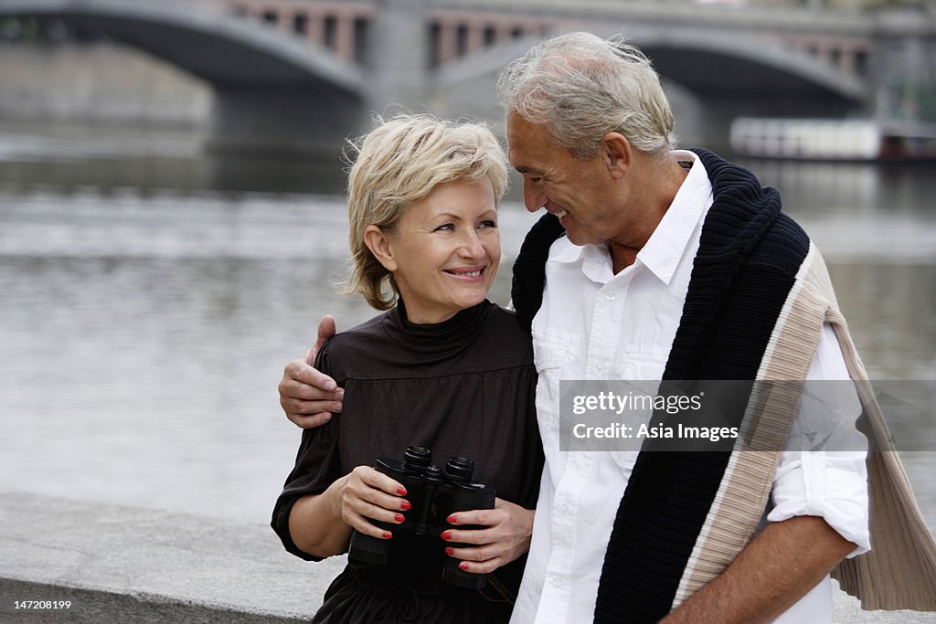 Mature couple sitting near bridge looking at each other and smiling