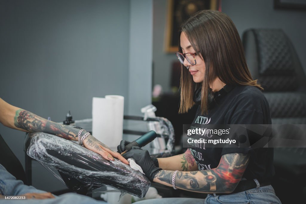 Kaukasische Tätowiererin, tätowiert die Kundin in ihrem Tattoo-Studio