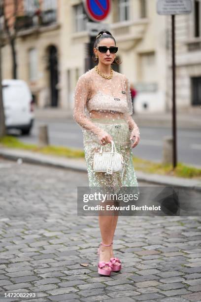 Bettina Looney wears a pink hair elastic, gold large hair clips, black sunglasses from Miu Miu, gold earrings, a gold and diamonds large necklace, a...