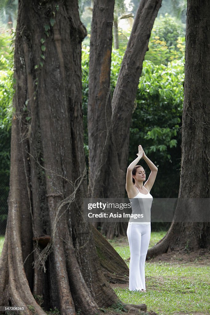 Young woman doing yoga under trees