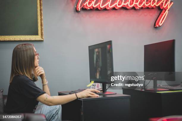 portrait of young tattoo master sitting at computer in tattoo studio choosing tattoo models. - paint microsoft stock pictures, royalty-free photos & images