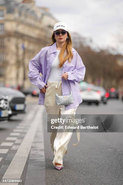 Merve Gorgotz wears a white with black embroidered logo cap from Miu Miu, purple sunglasses, gold and blue crystals earrings, a white ribbed...