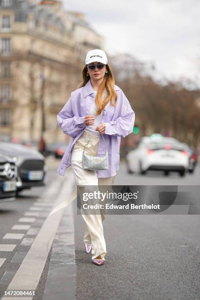 Merve Gorgotz wears a white with black embroidered logo cap from Miu Miu, purple sunglasses, gold and blue crystals earrings, a white ribbed...