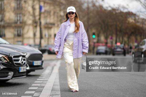 Merve Gorgotz wears a white with black embroidered logo cap from Miu Miu, purple sunglasses, gold and blue crystals earrings, a white ribbed...