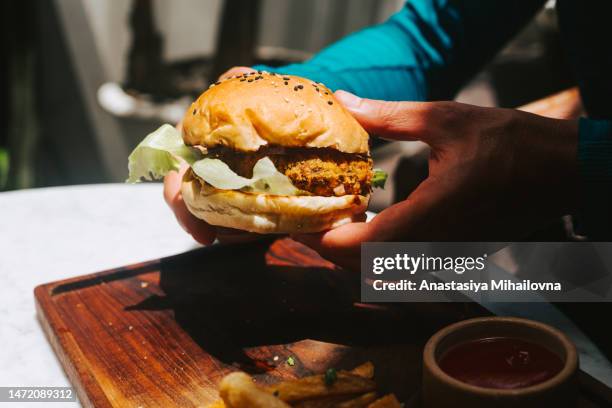 male hands holding vegan burger with bean patty - male burger eating fotografías e imágenes de stock