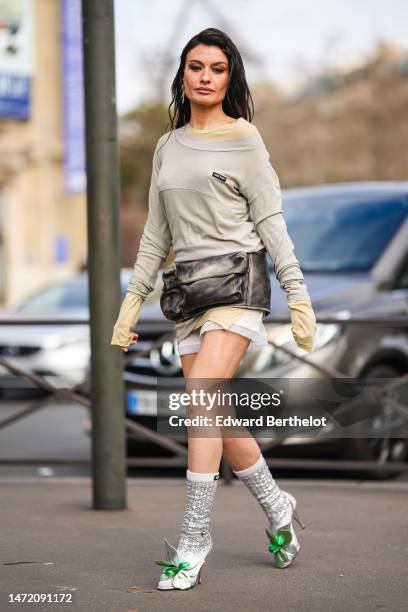 Angela Rozas Saiz wears gold pendant earrings, a pale yellow t-shirt, a pale gray long sleeves t-shirt short dress from Miu Miu, a black faded...