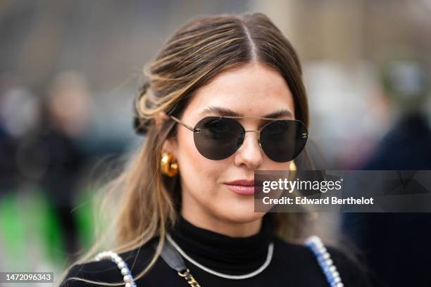 Paola Alberdi wears black sunglasses, gold earrings, a black wool turtleneck pullover, a rhinestones necklace, a royal blue and white tweed tank-top...