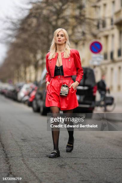 Xenia Adonts wears a black V-neck tank-top from Chanel, a red shiny leather cropped jacket from Chanel, a matching red shiny leather short skirt, a...