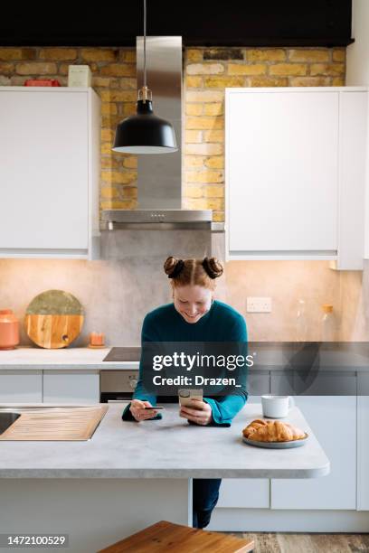 young redhead woman behind kitchen counter using phone and credit card - northern european stock pictures, royalty-free photos & images