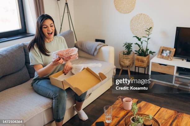 fröhliche frau öffnet ein paket, das an ihrer heimatadresse angekommen ist, ihr gesicht zeigt, dass sie mit dem online-shopping zufrieden ist - box purse stock-fotos und bilder
