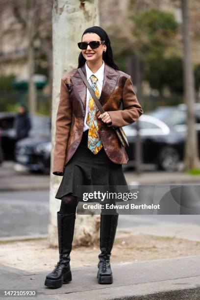 Maria Bernad wears a black large headband, a white shirt, a dark brown shiny leather embroidered yoke pattern blazer jacket, a dark brown shiny...