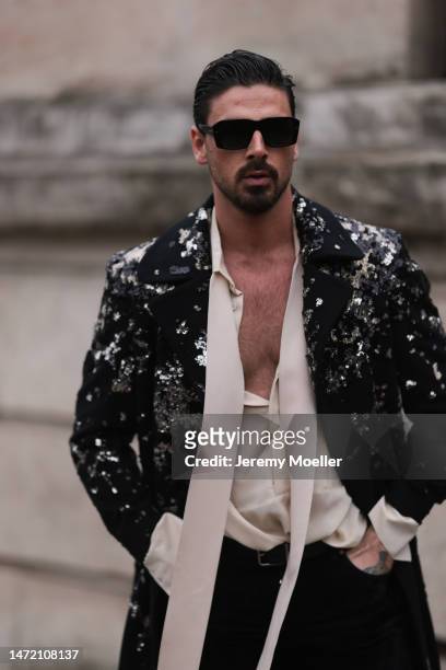 Michele Morrone wears Dolce & Gabbana black sunglasses, a black sequin suit jacket, a beige satin shirt with a scarf detail, black pants and a black...