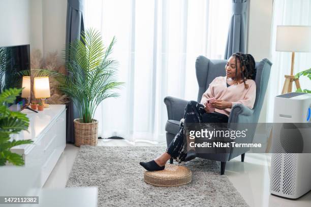 watching tv to chill out and reduce stress and improve your mental health after work. full length of african american young women watching online movies from the smart tv while sitting comfortably on the sofa in the living room. - air purifier fotografías e imágenes de stock