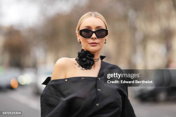 Justyna Czerniak wears black sunglasses, black earrings, a black ruffled flower large necklace, a black shirt, outside Awake, during Paris Fashion...