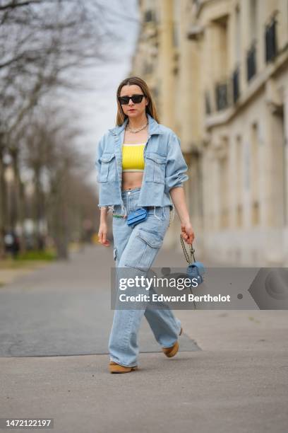 Julia Comil wears black sunglasses, silver earrings, a gold large chain necklace from Tiffany, a yellow ribbed cropped tank-top, a blue faded denim...