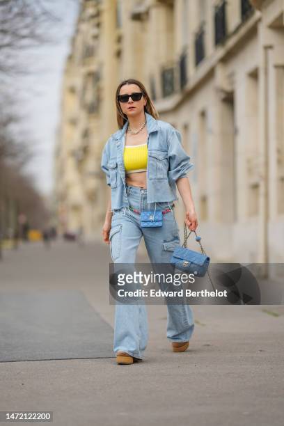 Julia Comil wears black sunglasses, silver earrings, a gold large chain necklace from Tiffany, a yellow ribbed cropped tank-top, a blue faded denim...