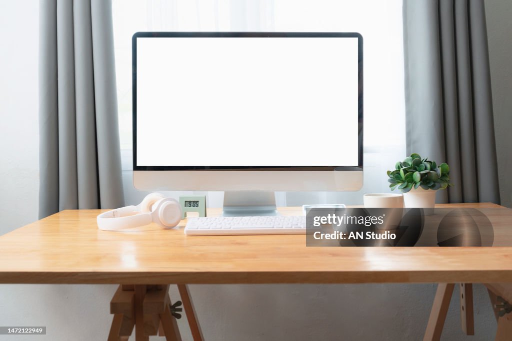 Front view of stylish workspace with mock up computer and office supplies gadget. Blank screen for graphic display montage. Blank screen desktop computer in minimal office room with decorations and copy space.