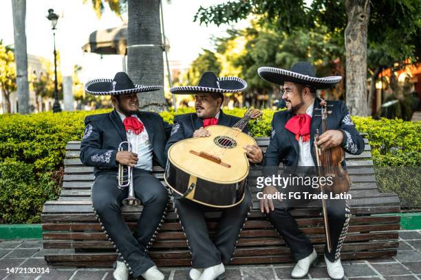 trio of traditional mariachis sitting on a bench outdoors - traditional music stock pictures, royalty-free photos & images