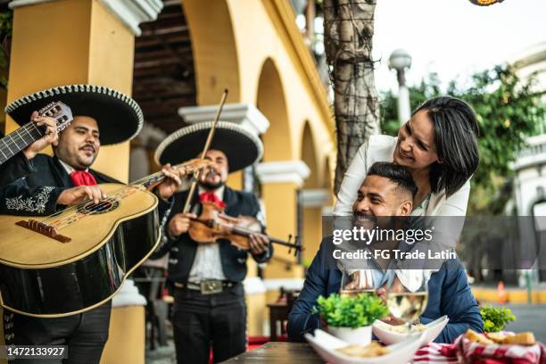 married couple listening to mariachi music at a restaurant outdoors - een serenaden brengen stockfoto's en -beelden