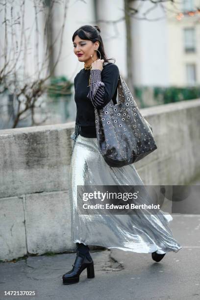 Maria Bernad wears silver and gold earrings, a gold large chain necklaces, a black pullover with embroidered silver fringed wrists details, a black...